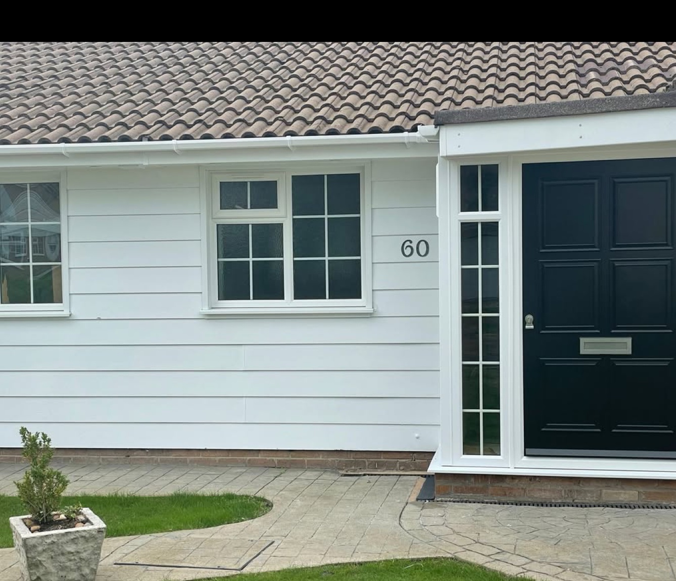 White-clad bungalow with cottage-bar windows and a navy front door